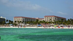 A beachfront hotel with multiple balconies, a sandy beach, and palm trees.