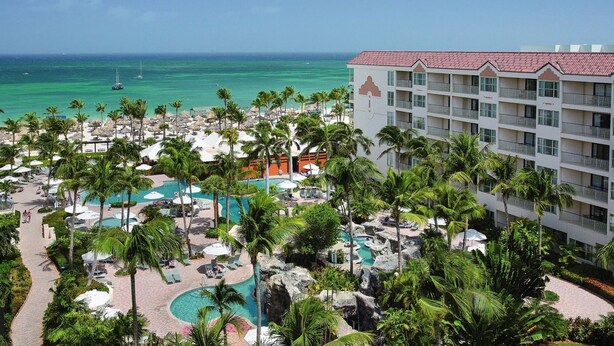 A resort with multiple swimming pools, palm trees, and a view of the ocean.