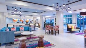 A spacious lobby with a modern design, featuring a seating area with sofas and chairs, a coffee table, and a reception desk.