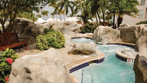 A pool area with large rocks, a bench, and a hot tub.