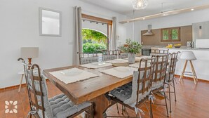 A modern dining area with a wooden table, grey upholstered chairs, and a hanging light fixture. - Villa FUMEPACOON by Abahana Villas (Benissa)
