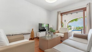 A modern living room with a flat-screen TV, comfortable seating, a glass coffee table, and a view of a pool and greenery. - Villa FUMEPACOON by Abahana Villas (Benissa)