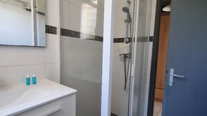 Moderni kylpyhuone, jossa on lasinen suihkuseinä, valkoinen allaskaappi, jonka päällä on kaksi shampoopulloa, sekä peili allaskaapin yläpuolella.