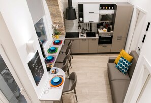 A compact kitchen with modern appliances, a dining area with colorful plates, and a cozy seating area with a sofa and cushions.