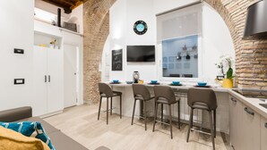 Une cuisine moderne avec un mur en briques en arc de cercle, un îlot central intégré avec des tabourets de bar et une horloge au mur.