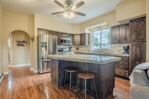 A modern kitchen with a large island, stainless steel appliances, wooden cabinets, and a ceiling fan. - Ladybug III: Fire Pit, Bikes & Dog Friendly (Fruita)
