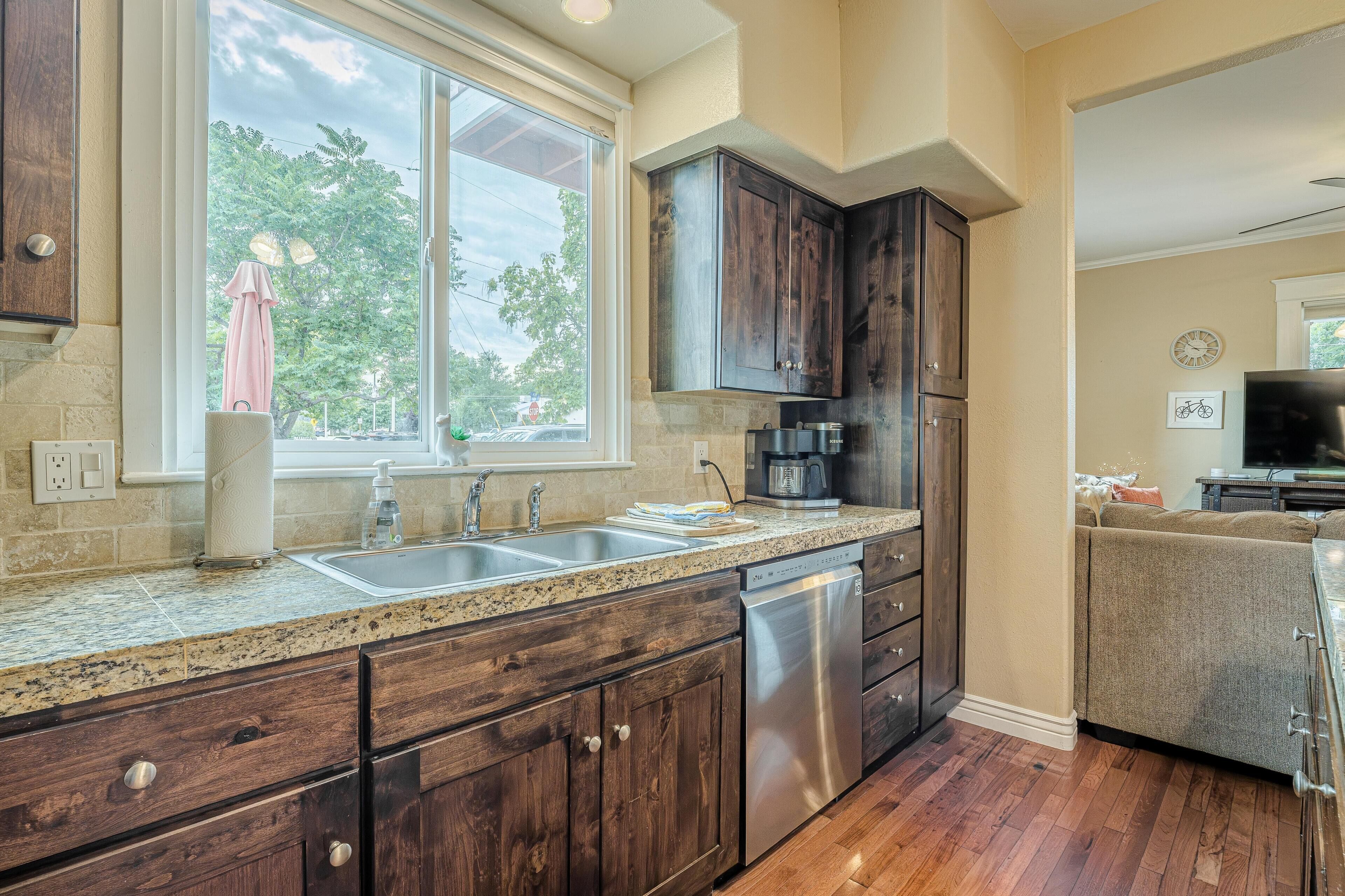A kitchen with dark wooden cabinets, a granite countertop, stainless steel appliances, and a window with a view of trees.