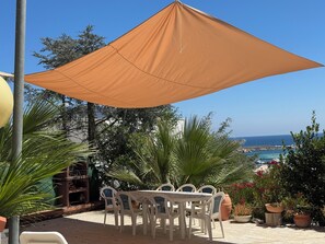 An outdoor patio with a table and chairs, a large umbrella, and a view of the sea. - VILLA NICE SAN VITO LO CAPO (San Vito Lo Capo)