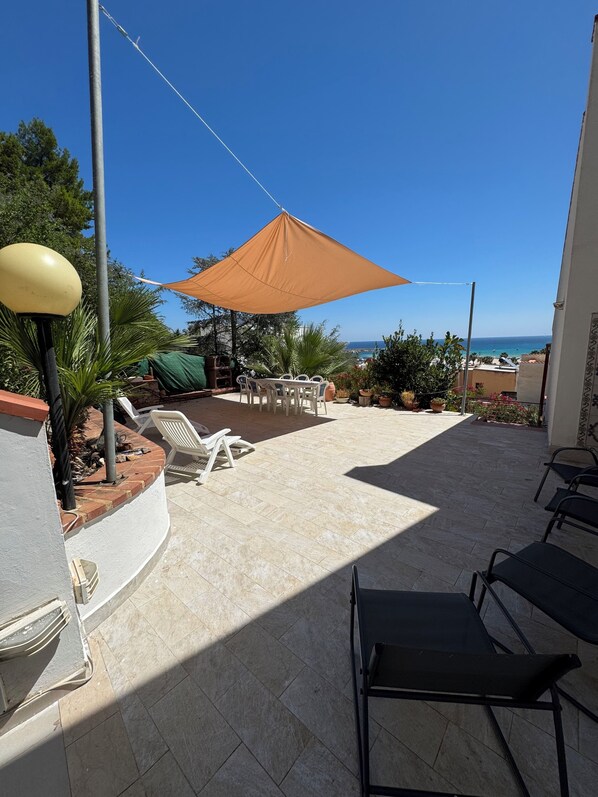 A patio area with a table and chairs, a large umbrella, and a view of the sea. - VILLA NICE SAN VITO LO CAPO (San Vito Lo Capo)