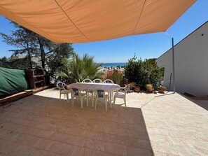 A covered outdoor dining area with a view of the sea, surrounded by potted plants and a white wall. - VILLA NICE SAN VITO LO CAPO (San Vito Lo Capo)