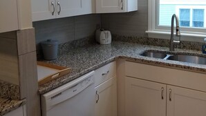 Eine Küche mit weißen Schränken, einer Granit-Arbeitsplatte, einem Geschirrspüler, einem Toaster und einem Fenster mit Blick ins Freie.