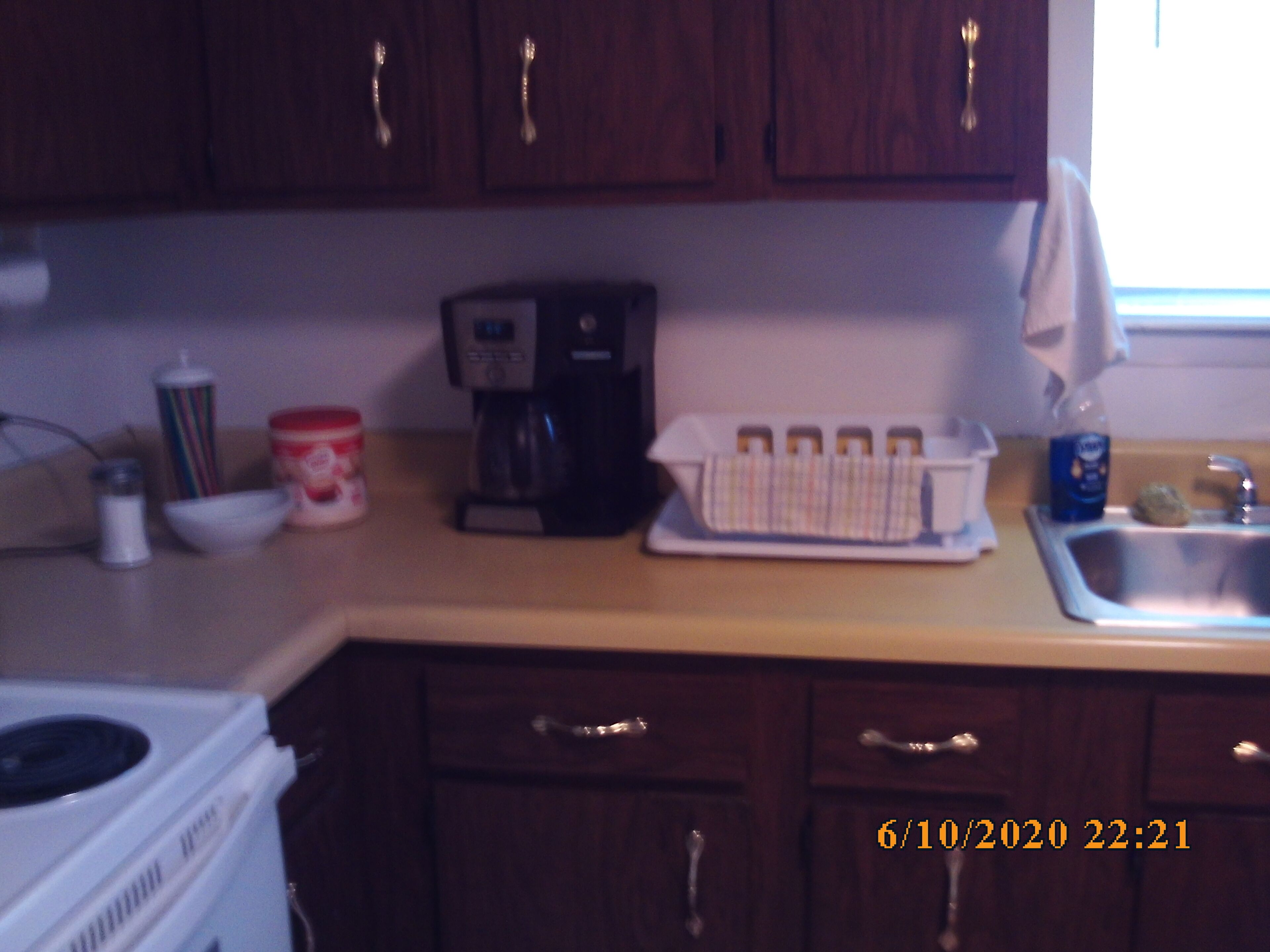 A kitchen with wooden cabinets, a coffee maker, a kettle, and a sink.