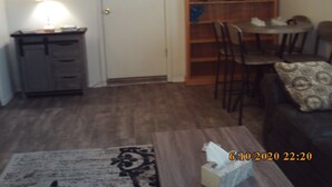 Un salon comprenant un canapé, une table basse, une table à manger avec des chaises, une bibliothèque et une porte.