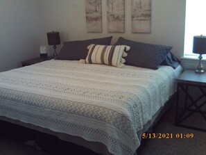 Uma cama bem arrumada com um cobre-leito estampado, duas almofadas e uma mesa de cabeceira com abajur.