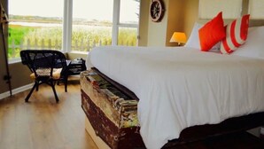 Un dormitorio con una cama grande, una silla, una lámpara y vistas al exterior.