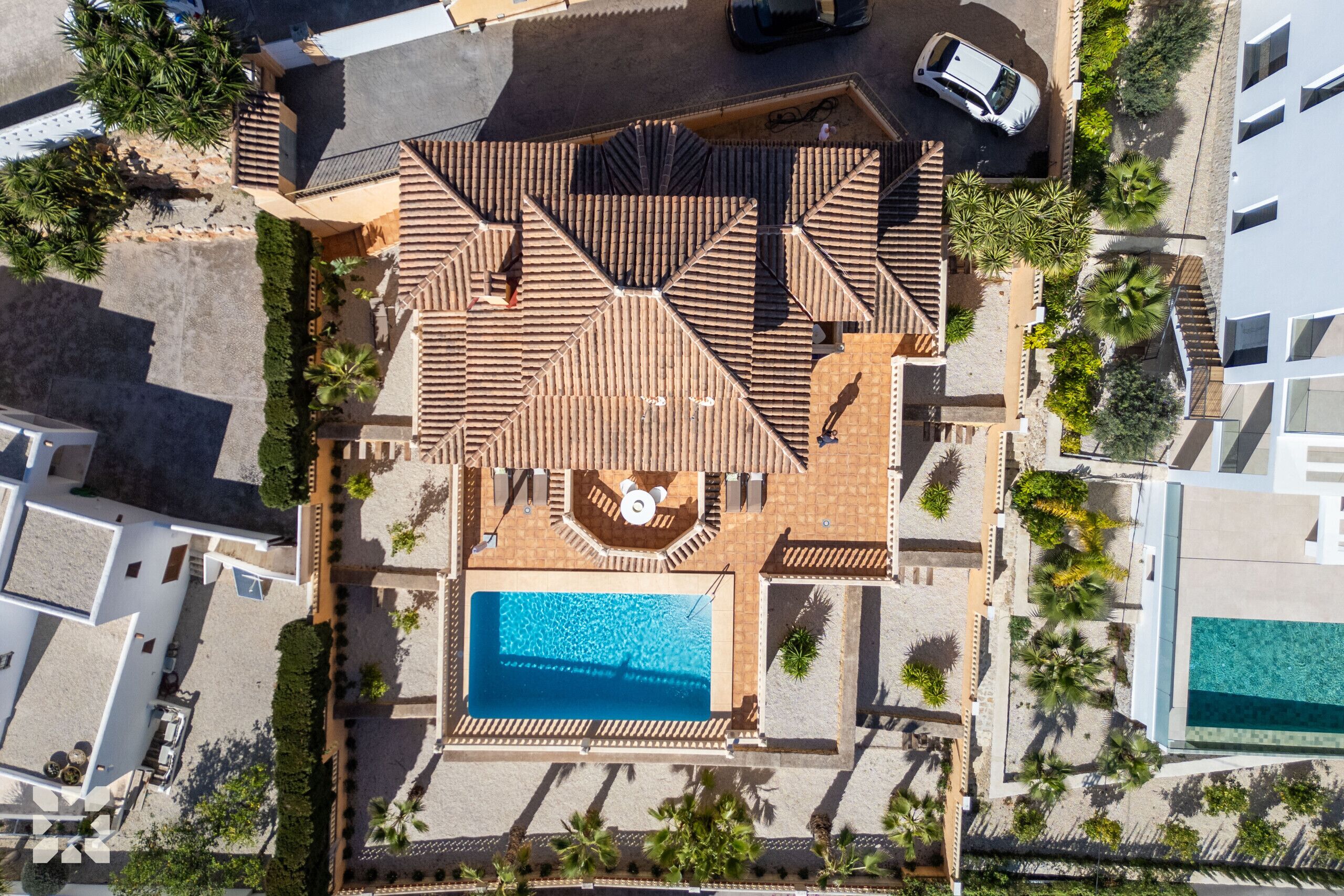 An aerial view of a residential area with a swimming pool, a tiled roof, and surrounding greenery.
