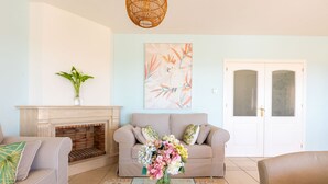 Ein Wohnzimmer mit einer Couch, einem Kamin, einer Blumenvase und einem Wandbild mit Vögeln.