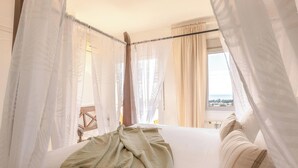 Ein Bett mit grüner Decke, weißen Vorhängen und Blick ins Freie.