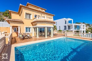 Une maison à deux étages avec une piscine, un balcon et un patio aménagé avec des chaises.