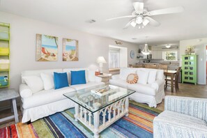 A living room with white sofas, a glass coffee table, and colorful striped rugs.
