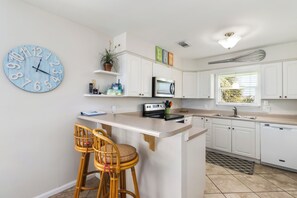 A kitchen with white cabinets, a microwave, a coffee maker, a clock, and a bar stool.