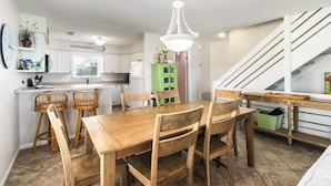 Et moderne køkken med hvide skabe, et spisebord med træstole, et grønt skab og en trappe.