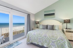 Ein Schlafzimmer mit einem großen Bett, einem Nachttisch, einer Lampe und Blick auf den Strand.