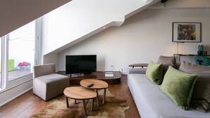 A modern living room with a flat-screen TV, a sofa with green cushions, a small wooden coffee table, and a cowhide rug.