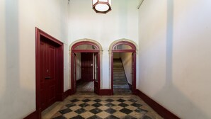 A hallway with checkered flooring, red doors, and arched doorways leading to another room.