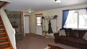 A living room with a brown leather sofa, a wooden staircase, a stone fireplace, and a hanging coat rack. - The Ranch House Retreat (Alton)