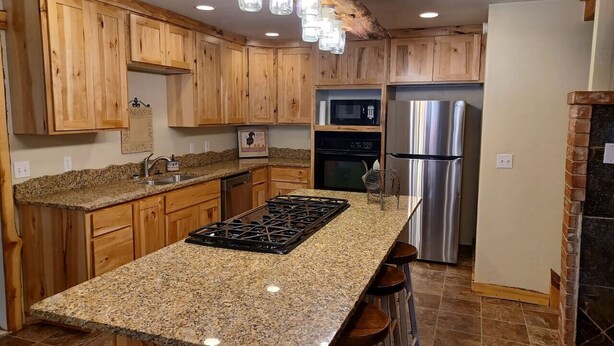 A kitchen with wooden cabinets, granite countertops, stainless steel appliances, and a central island with stools. - The Ranch House Retreat (Alton)