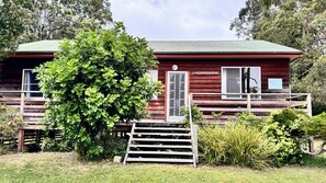 A cabin with a red exterior, a wooden deck, and a staircase leading to the entrance. - Riverwood - nestled beside the Wooli River (Wooli)