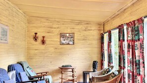 A wooden-paneled room with two wicker chairs, a small round table, and a window with patterned curtains. - Riverwood - nestled beside the Wooli River (Wooli)