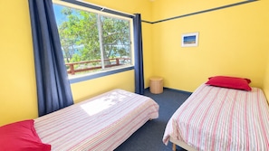 A room with two beds, a window with curtains, a small stool, and a picture on the wall.