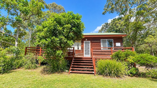 A wooden cabin with a staircase leading to the entrance, surrounded by lush greenery.