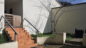 Eine Treppe führt zu einem Gebäudeeingang, ein Betonpflanzgefäß und ein Baum im Hintergrund.