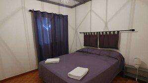 Ein Schlafzimmer mit einem Bett, einem Fenster mit Vorhängen, einem Nachttisch und einer Lampe.