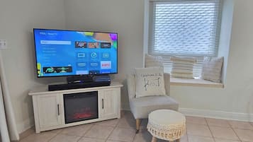 Una sala de estar con televisor, un mueble bajo, un banco junto a la ventana con cojines y un taburete decorativo.
