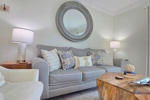 A living room with a grey sofa, two side tables, a round mirror, and a wooden coffee table. - Dog-Friendly Gulf Townhome · Steps to Sandy Beach (Port St Joe)