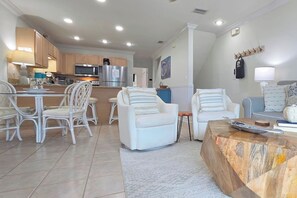 Una cocina moderna con armarios blancos, un comedor con sillas blancas y una sala de estar con un sofá y sillones.