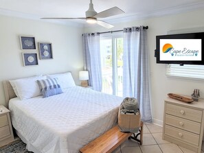 Une chambre à coucher comprenant un lit, une table de chevet, une commode, une lampe, un banc, un téléviseur, une fenêtre avec des rideaux et des œuvres d’art encadrées accrochées au mur.