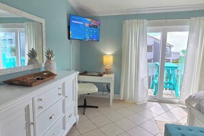 A hotel room with a desk, a TV mounted on the wall, a window with curtains, and a view of the outside.