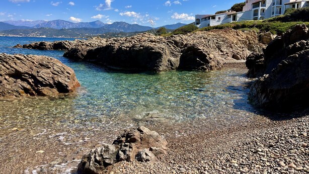 A coastal scene with clear water, rocky shore, and a building with balconies overlooking the sea. - 4-person apartment in the heart of the pevani estate (CALCATOGGIO)