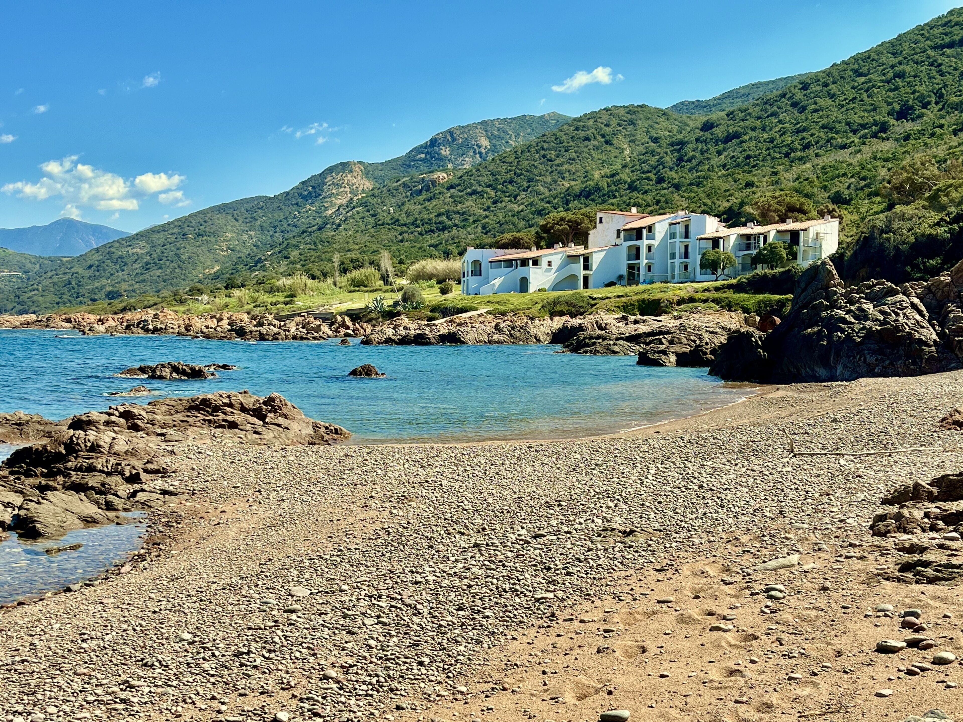 A coastal property with a rocky beach, clear blue waters, and a mountainous backdrop.