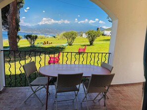 Ein überdachter Außenbereich mit einem runden Tisch und Korbstühlen, mit Blick auf eine grüne Landschaft und ein Gewässer.