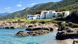 A coastal property with a white building featuring multiple balconies, situated on a rocky shoreline with clear blue water. - 4-person apartment in the heart of the pevani estate (CALCATOGGIO)