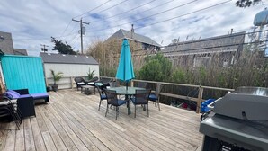 Eine Holzterrasse mit Tisch, Stühlen, einem blauen Sonnenschirm und einem Grill.