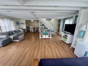 A spacious living area with a staircase, a dining table, and a television. - Fire Island Beach Haven (Ocean Beach)