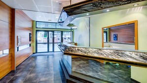 Un vestíbulo de hotel moderno con un mostrador de recepción de mármol, amplias puertas de cristal que dan al exterior y un techo con diseño perforado.