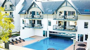 A hotel with a large outdoor swimming pool, multiple balconies with outdoor seating, and a modern architectural design.